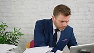 Premium stock video - A stressed businessman using a calculator to add up bills and taxes with piles of paperwork