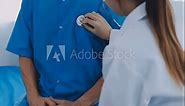 Caring female nurse in medical facemask listen to elderly patient heart with stethoscope in hospital. Woman GP or doctor in facial mask do checkup examine mature man client on consultation in clinic.