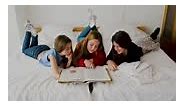Cute Little Girls Reading A Book And Smiling While Lying On Bed In...