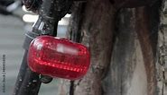 Bicycle red flashing LED tail light. The back of a velobike parked near a tree with flashing red light footage. Bicycle flasher in action.