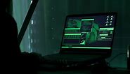 Premium stock video - A criminal hackergirl with black hood using laptop and big computers to hack network system from her dark hacker neon room