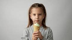 Cute little girl enjoys a delicious ice cream cone. Child with ice cream on a white background, 4k