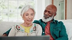 Old couple on sofa with laptop, smile and relax with love, interracial marriage and online bonding in home. Computer, streaming website and happy people, senior man and woman on couch in living room.