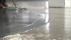 Low Angle Closeup Construction Worker Applying Gray Liquid Cement Solution Coating On Concrete Floor With Squeegee,Spike Boots Floor Leveling