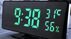 Digital Clock Showing Time on Green Display 9:39 AM, Temperature, Air Humidity. Modern mirror clock, alarm clock with a thermometer, hydrometer standing on a desk on white background. Time concept.