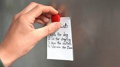 close-up of a man sticking a piece of paper with a to-do list on the fridge