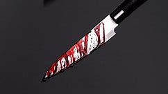 4K footage Close-up Front view, Bloody kitchen knife with drops of blood flowing along the sharp blade isolated on black background.