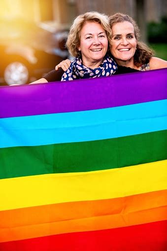 Smiling Happy Mature Lesbian Couple Posing Holding A Rainbow Flag Stock