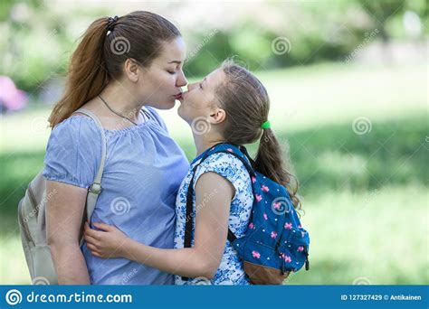 mother kissing her daughter while walking summer park