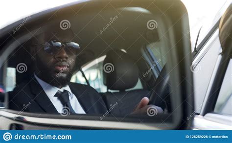 black man in sunglasses driving car looking in side view mirror