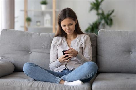 smiling woman sitting on sofa using mobile phone looking at screen