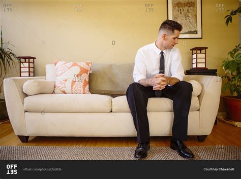 Man Sitting Alone On A Couch With His Hands Clasped Together Stock