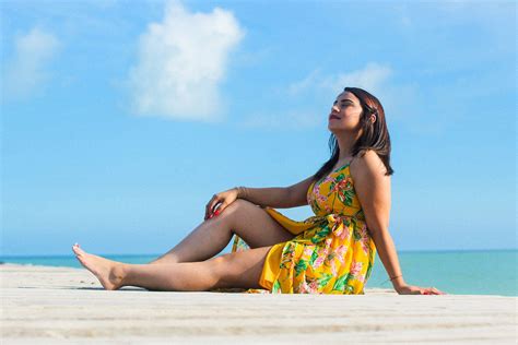 A Woman In A Yellow Dress Sitting On The Beach Looking Up At The Blue Sky