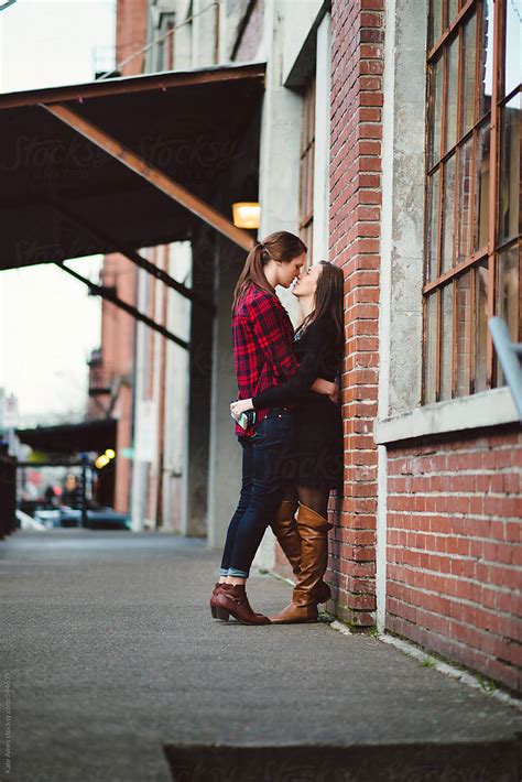 lesbian couple embrace against brick wall during a date downtown by
