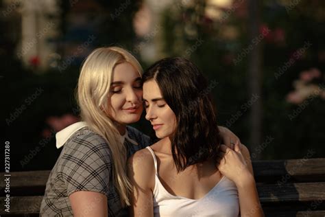 Blonde And Brunette Lesbians Holding Each Other Sitting On Bench
