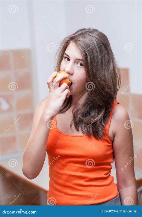 Девочка подросток в оранжевой футболке есть персик Стоковое Фото