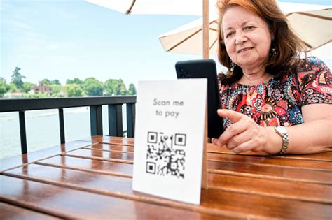 mature hispanic woman scanning a qr code with her phone to pay cashless