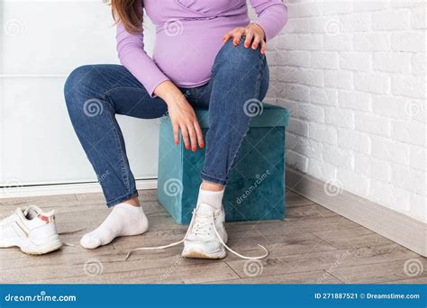 a pregnant girl with a big belly puts on sneakers on her feet the