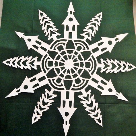 A Snowflake Made Out Of White Paper On A Green Tablecloth With Arrows