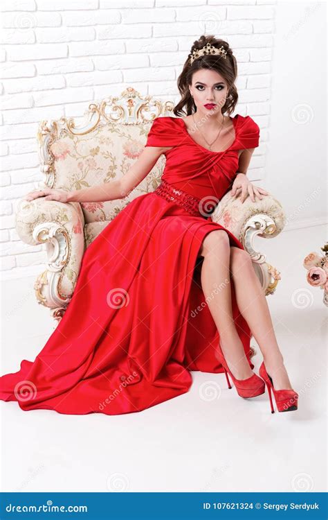 Elegant Woman In Long Red Dress Sitting On Vintage Chair In Whit Stock