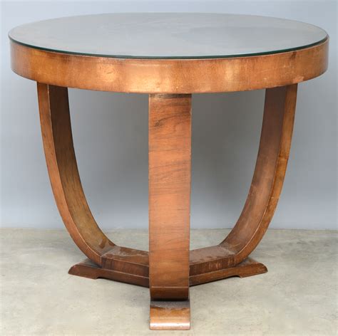 een ronde tafel op drie gebogen poten van gefineerd hout en met een glazen blad tijdperk art
