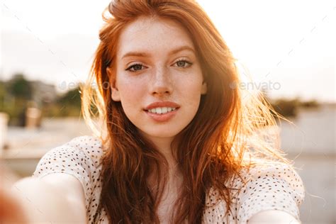 Image Of Pleased Ginger Girl Taking Selfie And Smiling At Camera Stock