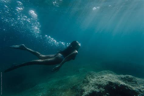 wide shot of a woman swimming underwater by stocksy contributor
