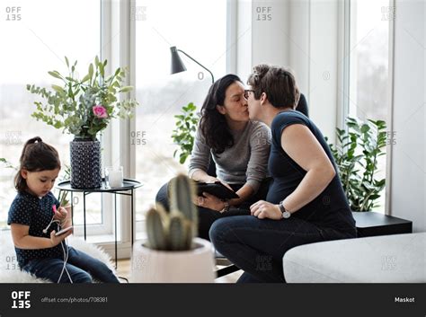 Lesbian Couple Kissing While Girl Using Mobile Phone In