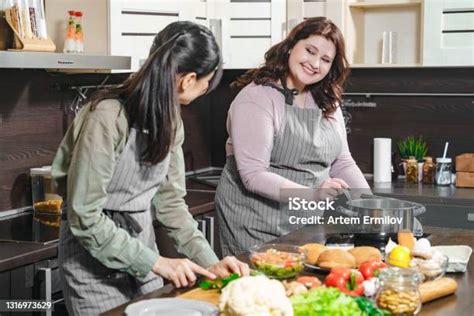 Two Young Cheerful Girlfriends Preparing Meal Together In The Home