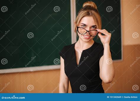 Young Female Teacher In Glasses Stand In Front Of Blackboard Stock