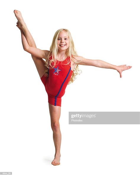 a little blonde girl in a red gymnastics outfit holds her leg high into