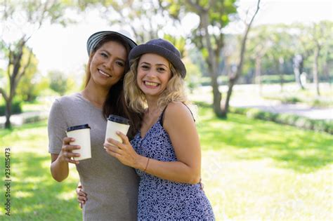 Excited Beautiful Lesbian Couple Hugging And Drinking Coffee In Park