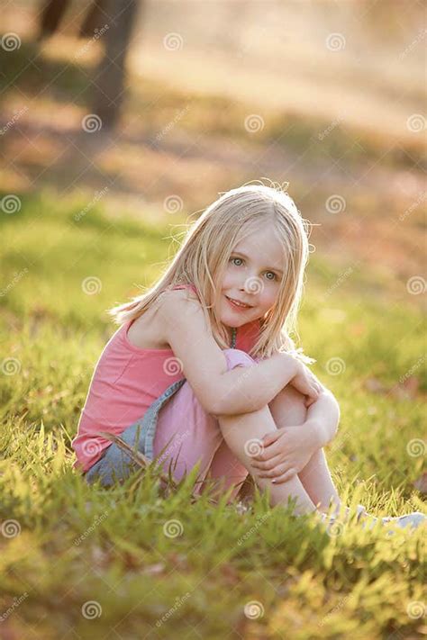 A Young Blonde Girl Sitting On The Grass In The Back Light In Summer