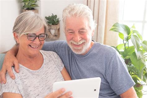 Senior Couple Smiling Looking At The Same Tablet Resting Embraced In