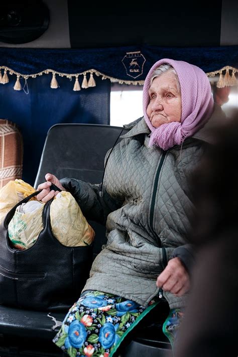 An Old Woman Sitting On A Bus With Her Handbag In Her Lap And Looking