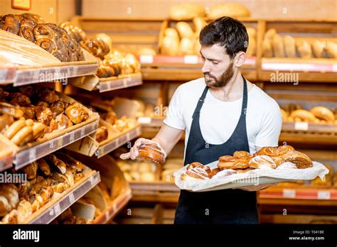 handsome baker  uniform putting fresh pastries   shelves