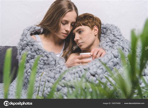 beautiful lesbian couple cup coffee embracing knitted wool blanket
