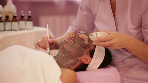 Massage Therapist Applying Cosmetic Mask On Female Face At Beauty Salon