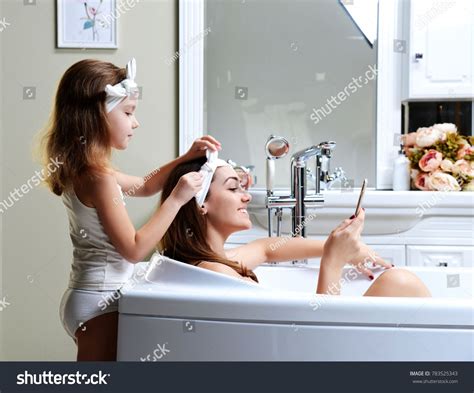 Young Mother And Daughter In A Bathroom Bath Tub Playing With Mobile