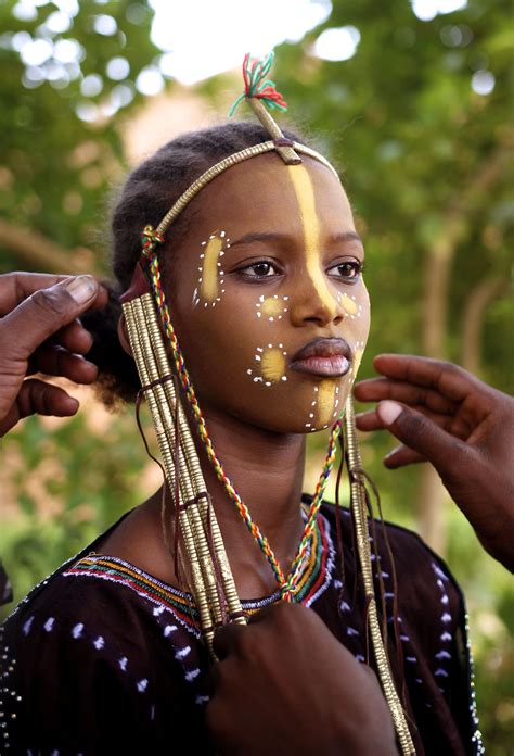 teenage girl is dressed in traditional fulani headgear and makeup by her father and uncle