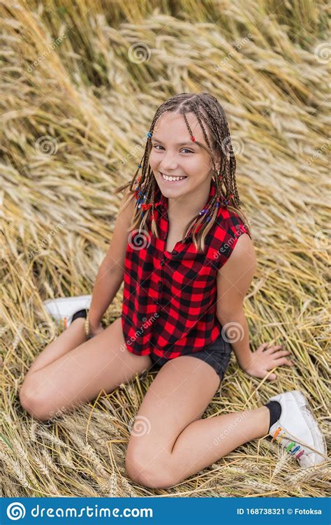 Smiling Teenage Girl With Braids Sitting In Wheat Field At
