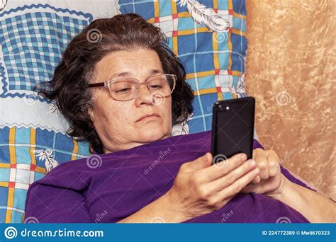 Elderly Woman Lying In Bed During Illness With A Phone In Her Hands