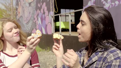 two funny teens hide behind donuts and makes silly faces then they feed each other bites 4k