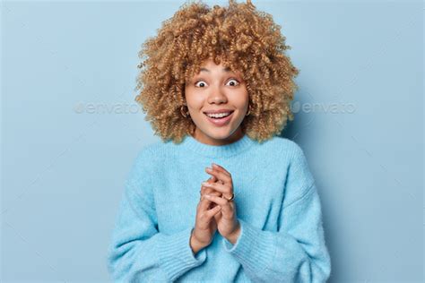photo of surprised curly haired woman stares amazed at camera smiles