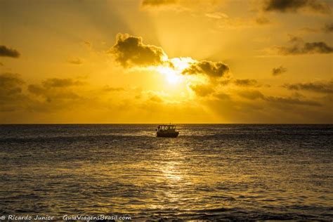 imagem do por do sol e um barco no mar da praia da conceição
