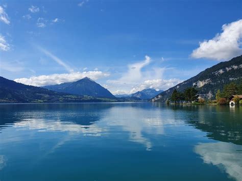 lake surrounded  mountains   blue sky  clouds   distance  houses   shore