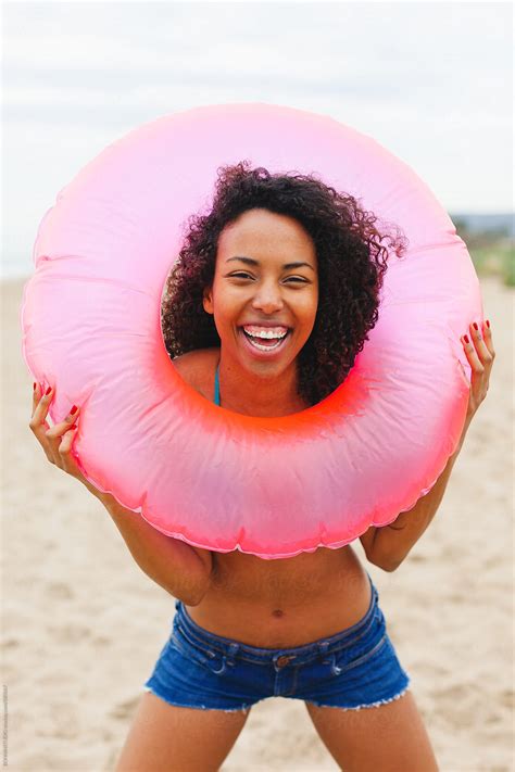 Happy African American Woman Holding A Pink Inner Tube On The Beach