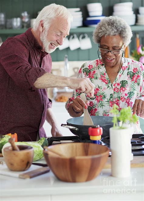 Active Senior Couple Cooking In Kitchen Photograph By Caia Image