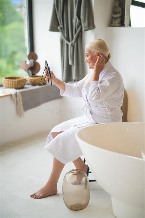 Pleased Mature Woman With The Mirror Sitting In The Bathroom Stock