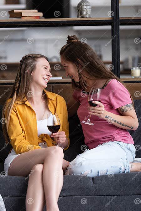 Two Smiling Lesbians Holding Wine Glasses And Looking At Each Other